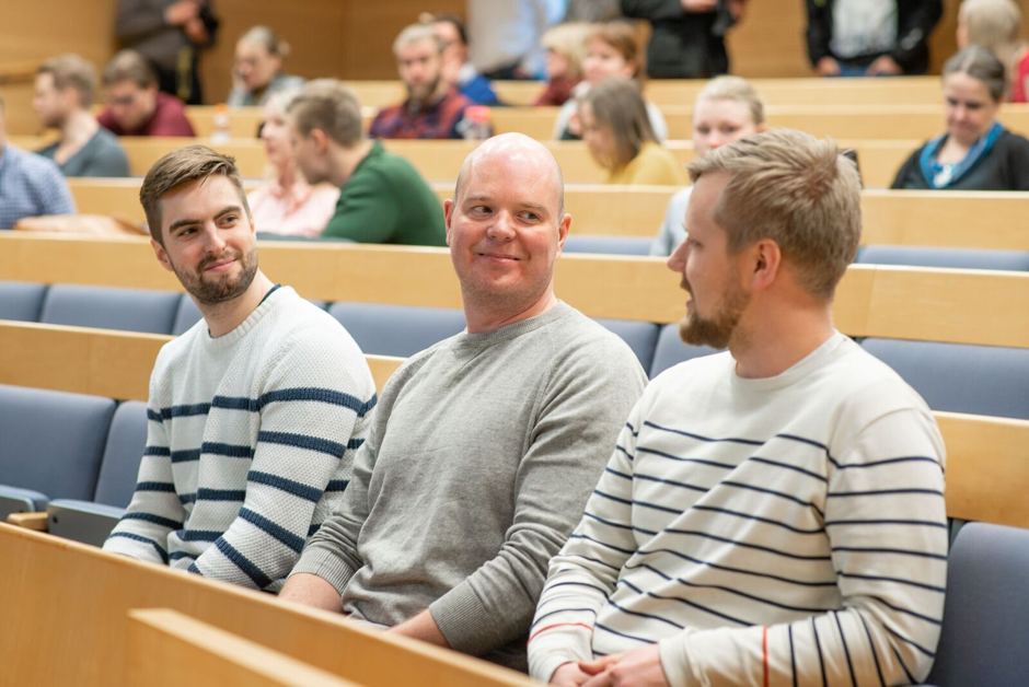 Luokkahuone, jonka etualalla istuu kolme opiskelijaa juttelemassa keskenään.